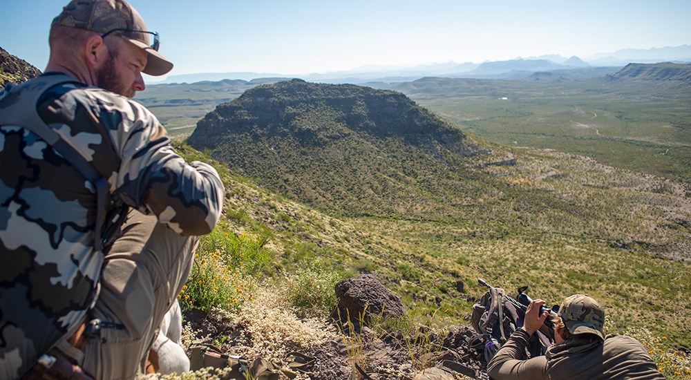 Male laying prone on side of steep hill preparing to shoot bolt action rifle.