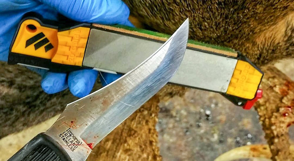 Fixed blade stainless steel knife running along manual knife sharpener.