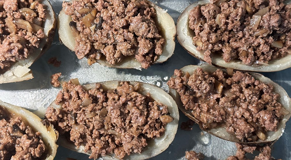 Venison meat mixture inside russet potatoes on baking sheet.