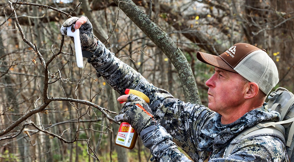 Hunter spraying deer scent on stick in tree.