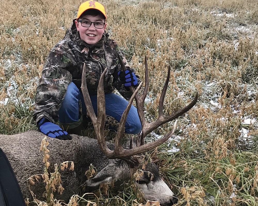 Youth male hunter with large mule deer buck.