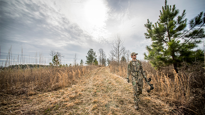 Hunter walking down trail with compound bow in hand