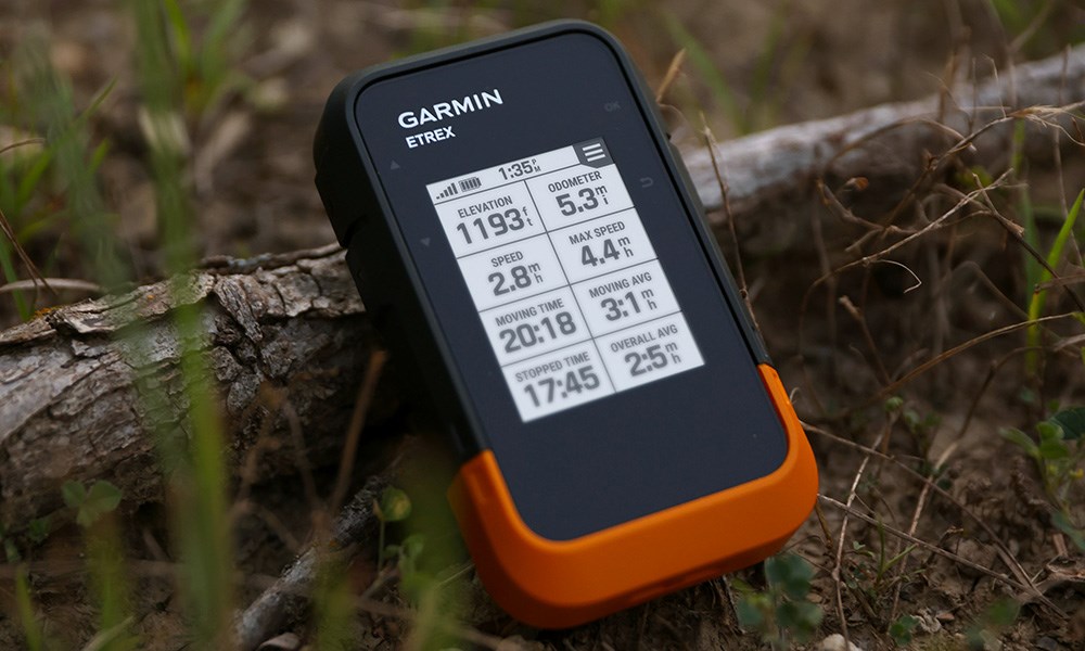 Garmin eTrex handheld GPS unit resting against forrest branch on the ground.