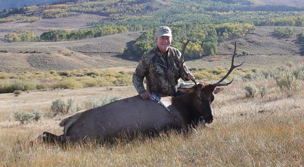 Male hunter posing with elk in Colorado mountains.