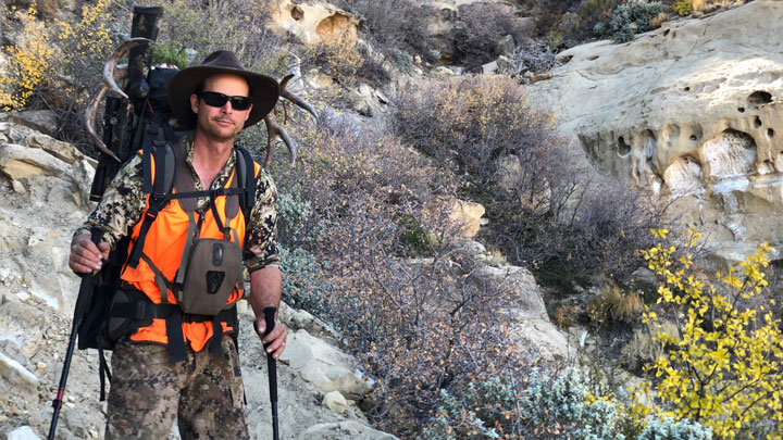 Backcountry hunter with pack uses trekking poles to hike over rocks