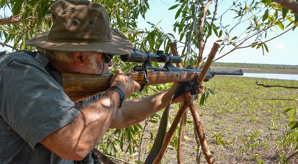 Man shooting dangerous game rifle off of shooting sticks in Africa