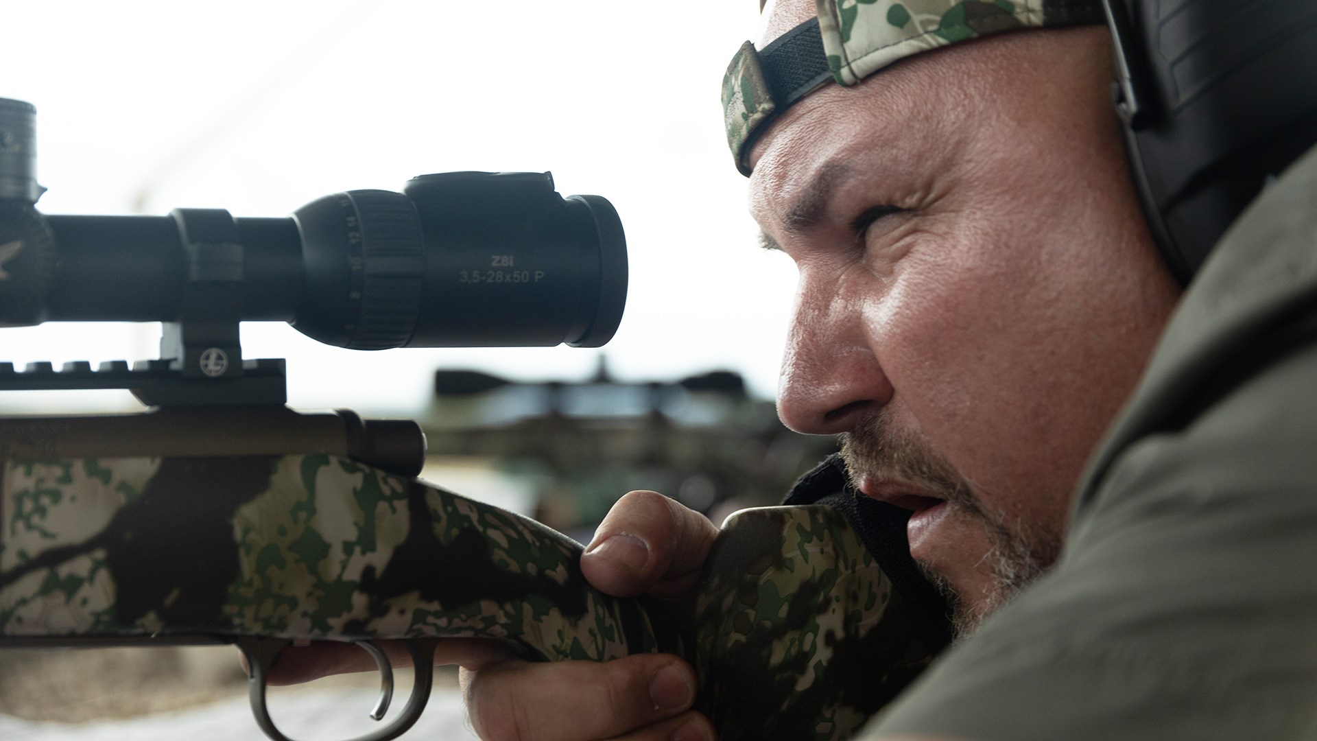 Male hunter looking through Swarovski riflescope preparing to shoot a bolt action rifle.