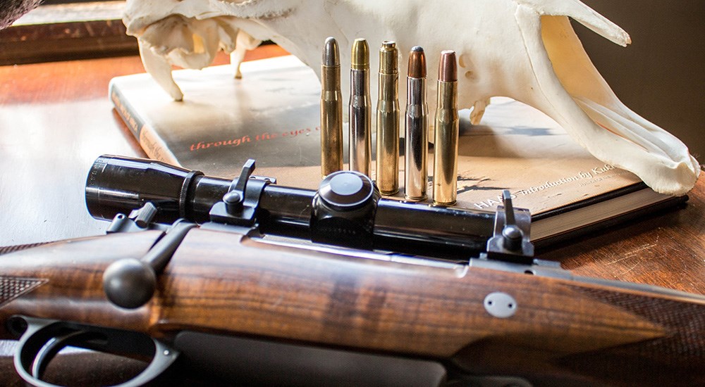 Five .404 Jeffery cartridges standing up on table next to bolt action rifle.