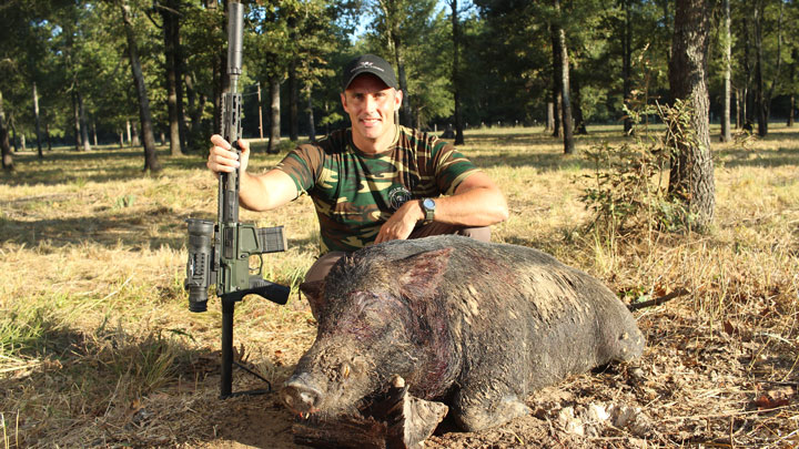 Hunter with rifle kneeling over dead pig.