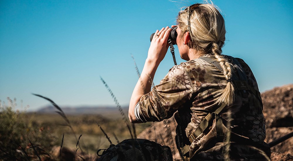 Female hunter looking through binoculars for aoudad in Texas.