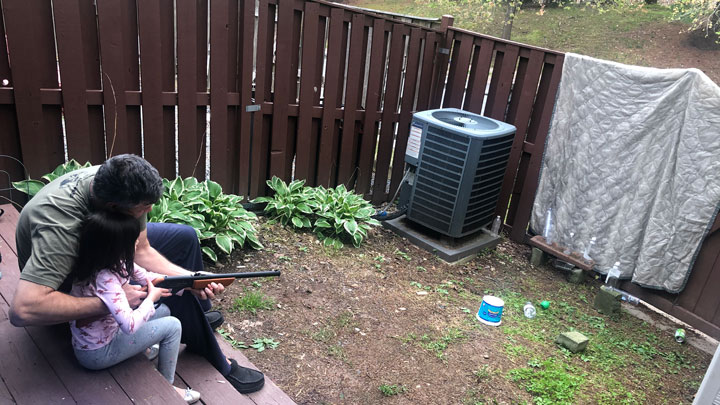 Max instructing his daughter on how to shoot a BB gun, in the backyard.