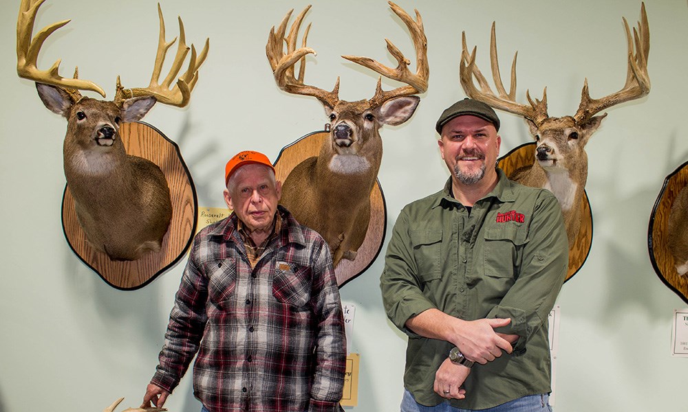 Two males standing in front of New York record whitetail buck mounts.
