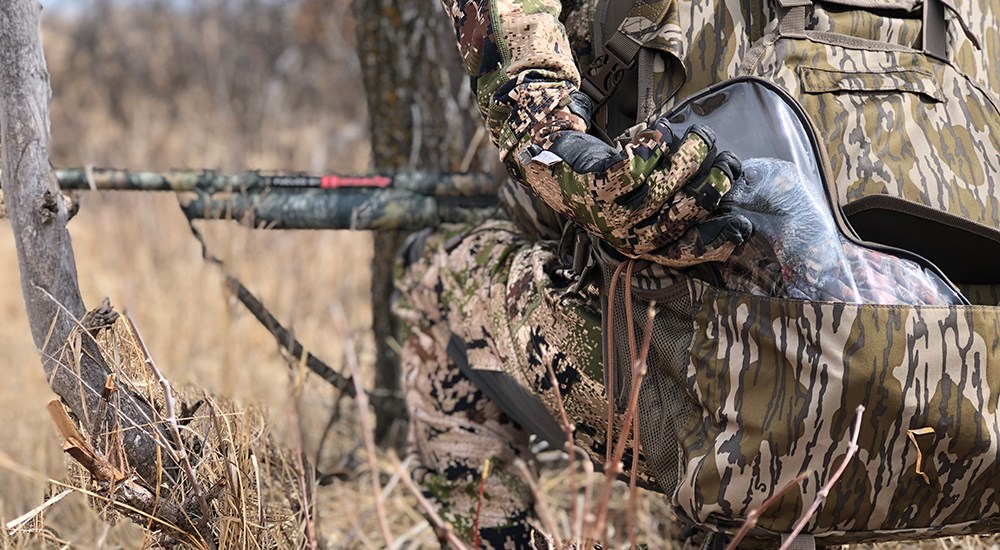 Hunter bent on ground using binocular to spot turkeys.