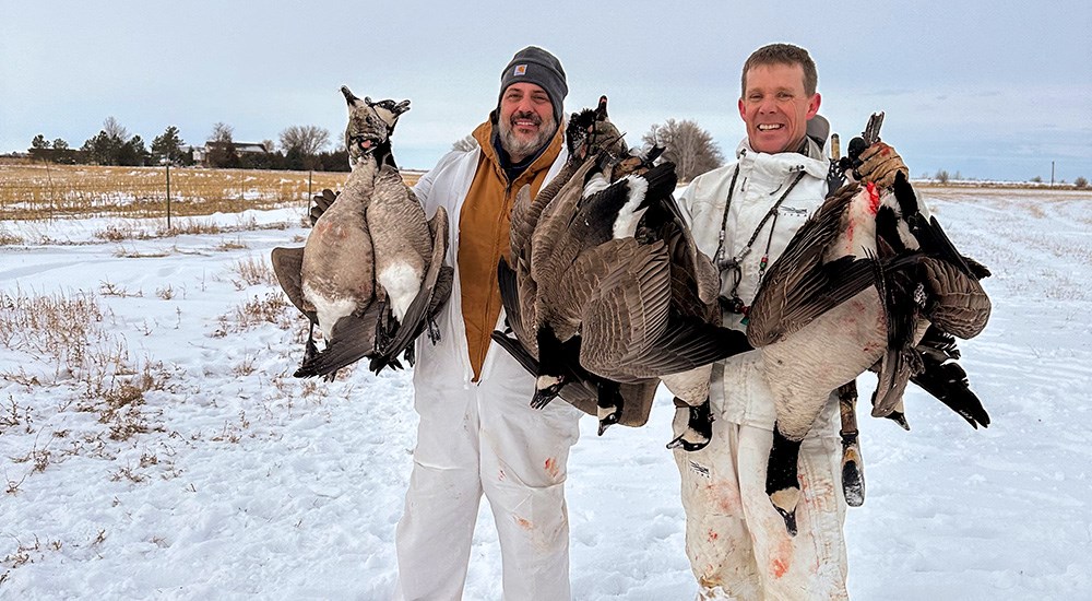 Male goose hunters holding up Canada geese in the snow.