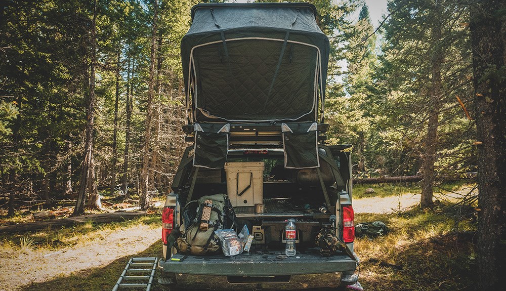 Rearview of truck bed with hard shell tent mounted on top in woods.