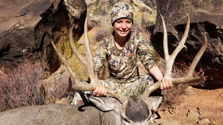 A huntress holds the antlers of a large buck