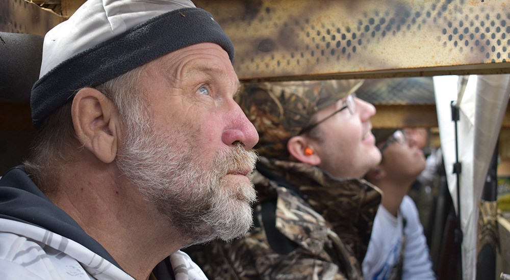 Male snow goose hunters in pit blind looking up.
