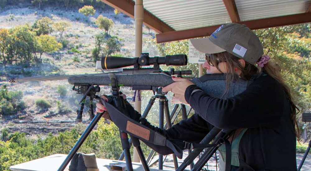 Female shooting bolt action rifle on shooting range.