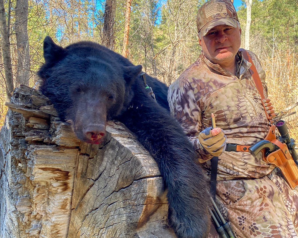 Hunter posing with black bear holding bullet.