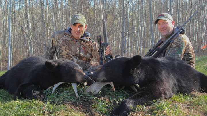 Two hunters kneeling over two dead black bears