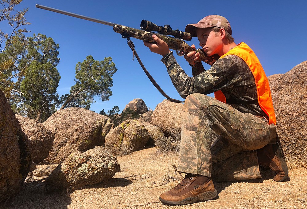 Teenaged male shooting rifle from kneeling position