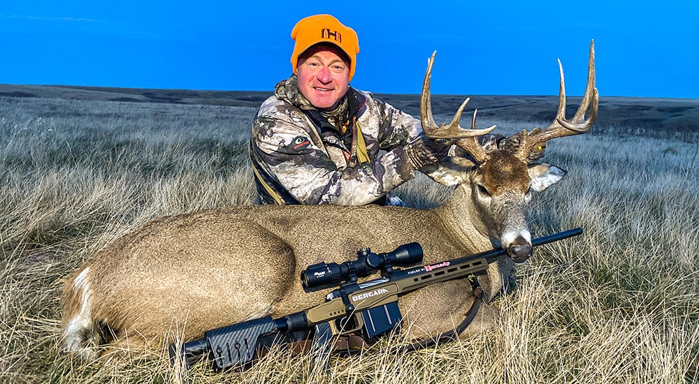 Male hunter posing with large whitetail buck in open field.