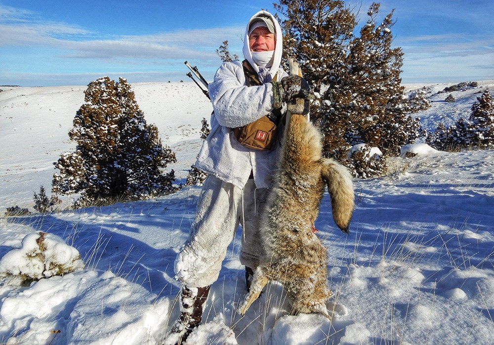 Male hunter holding coyote up on snow covered mountain.