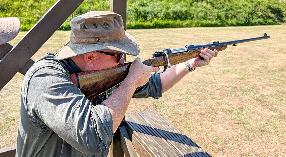 Male shooting .350 Rigby Magnum rifle on outdoor shooting range.