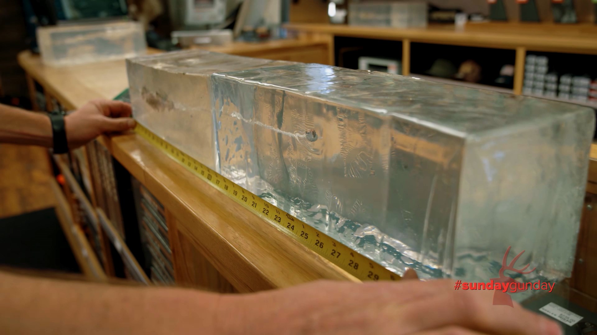 Man measuring ballistic gel with tape measure on desk arms outstretched clear gel bullet upset