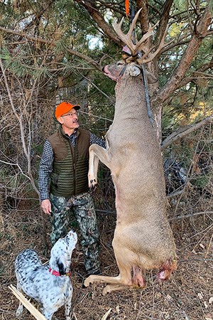 Hunter admiring white-tailed deer hanging on buck pole.