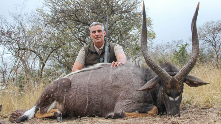 Hunter kneels behind a downed African animal with curved horns