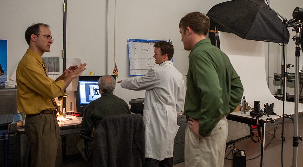 Four males in photography studio discussing edits on photos.