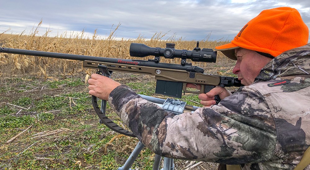 Male hunter shooting Bergara rifle off of shooting sticks in an open field.