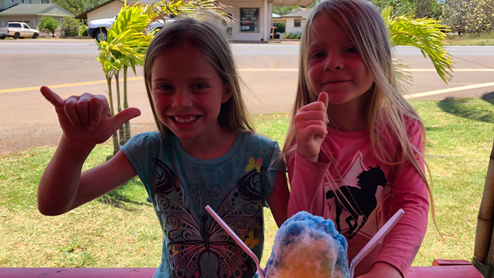 Two young girls enjoying shave ice, one throwing up the traditional Hawaiian, hang loose hand signal.