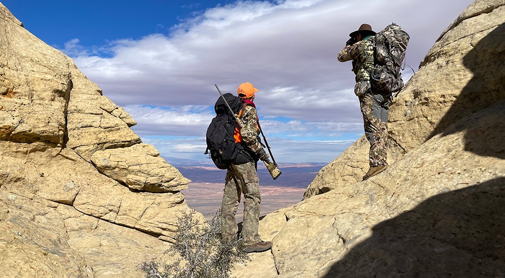 Two hunters on high rock vantage point.