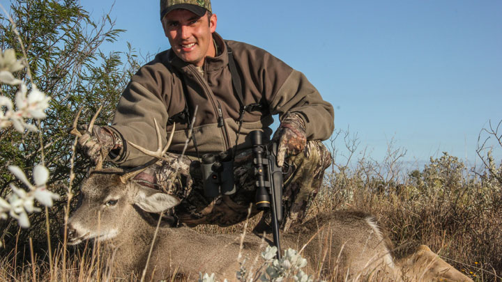 Hunter kneeling behind a dead whitetail