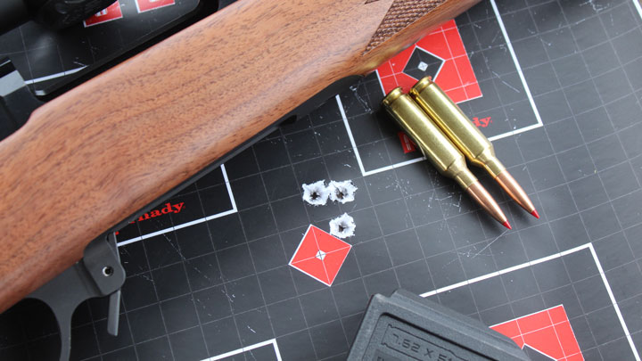 Two 6mm Creedmoor Cartridges laying next to three shot group with rifle above.