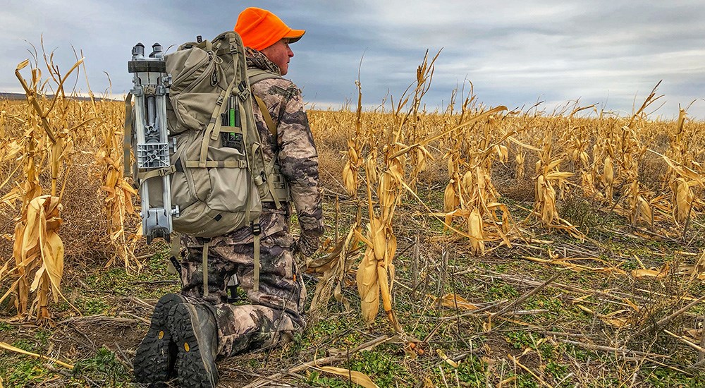 Male hunter bent down on his knees in a corn field.