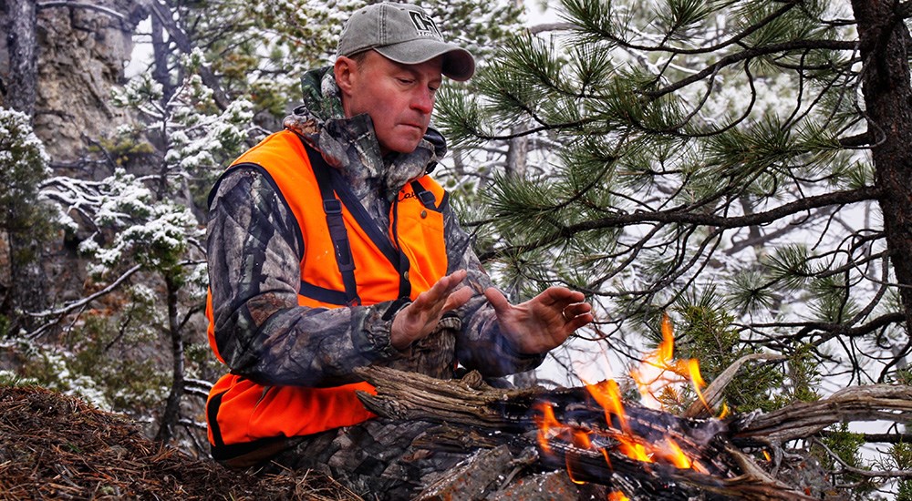 Man in camouflage warming up by a fire in the woods.