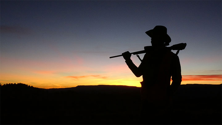 Hunter carrying rifle on shoulder at dusk