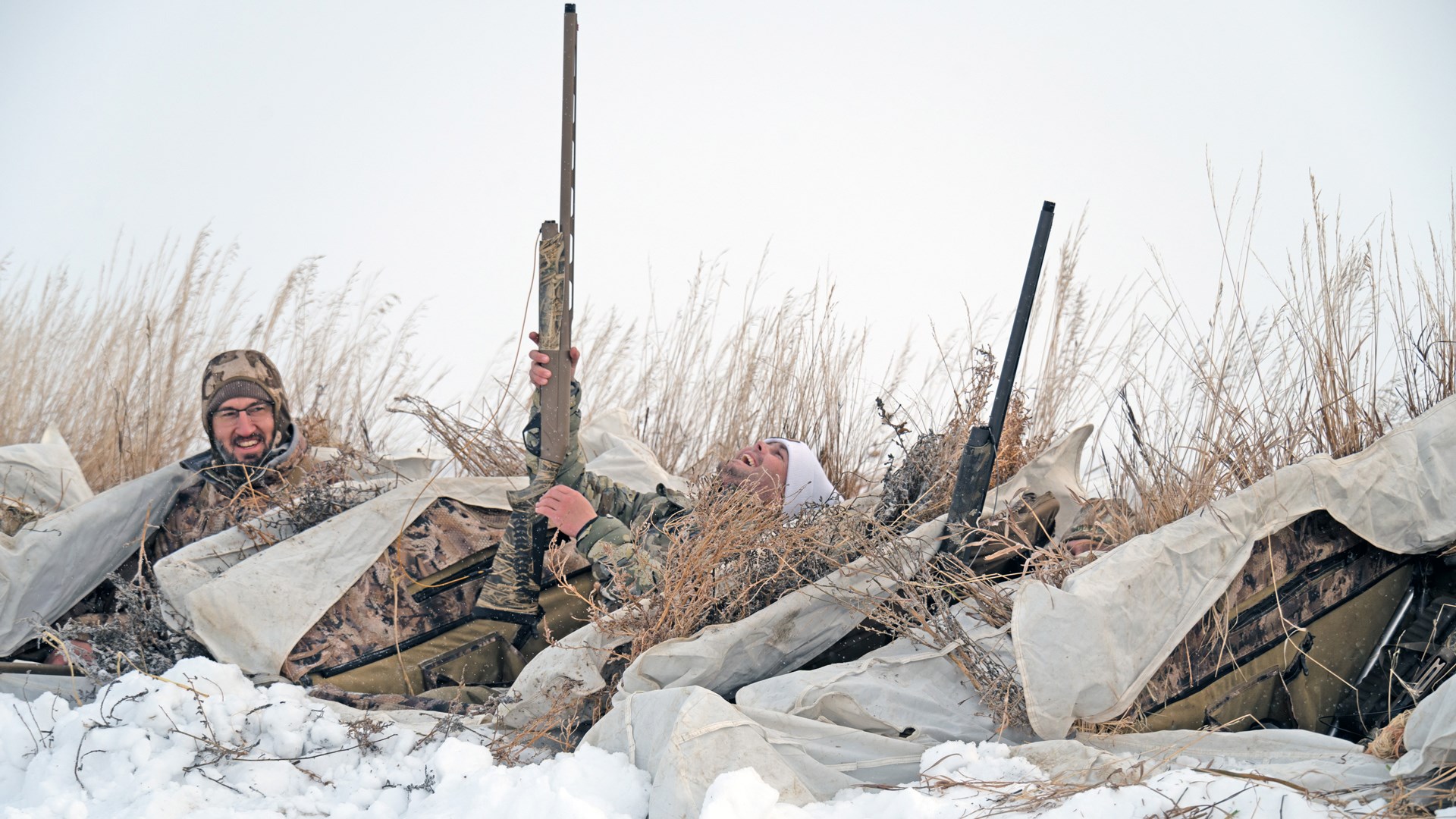 Happy hunters in snow grass holding shotguns goose hunting overcast sky