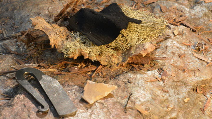 Piece of char cloth in a tinder nest, next to a striker.