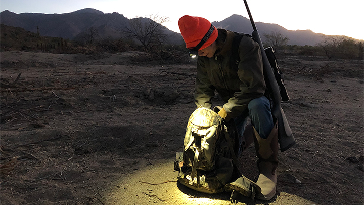 Hunter wearing headlamp to search backpack for tools