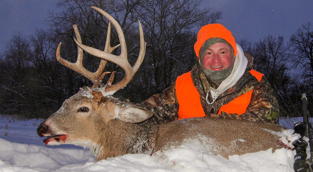 Male hunter posing with large whitetail buck in snow.