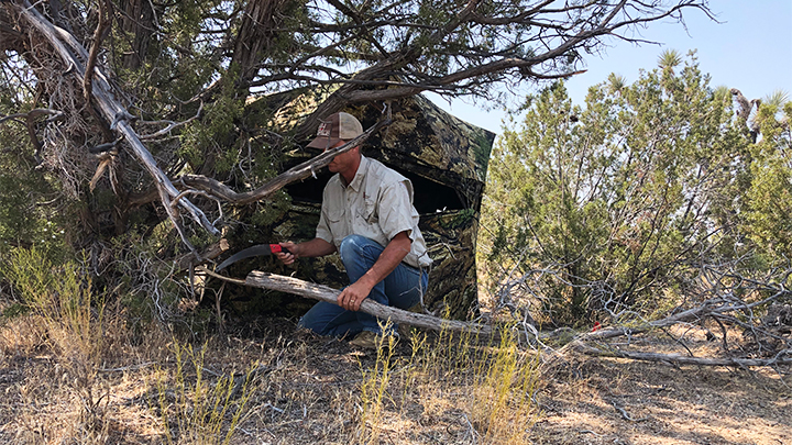 Hunter clearing shooting lanes for bowhunting ground blind