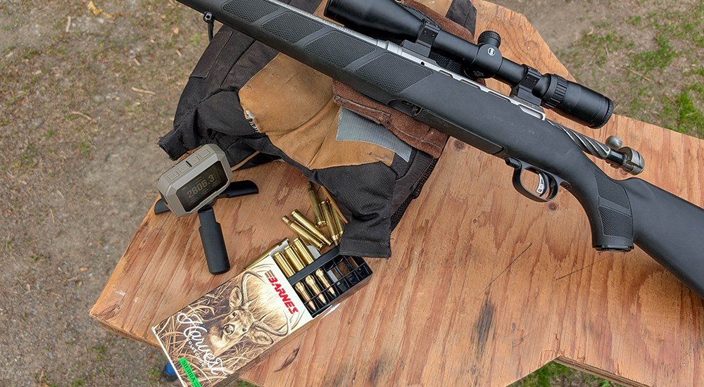 Barnes bullets with Savage rifle on wood bench at shooting range.