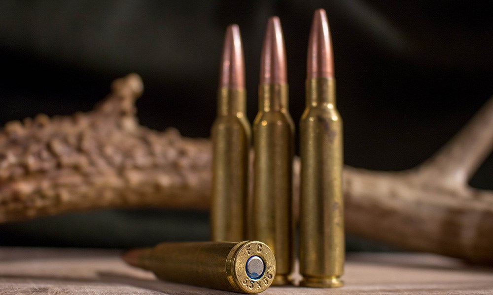 Four rifle cartridges on table with one showing 6.5x55 Swedish head stamp.