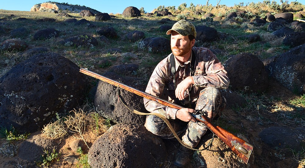Hunter holding rifle on mountain terrain.