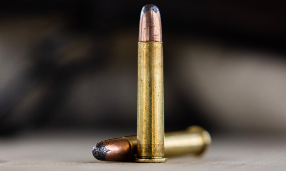 Two 360 Buckhammer ammunition cartridges, one standing and one laying on its side angled left, on black texture background.