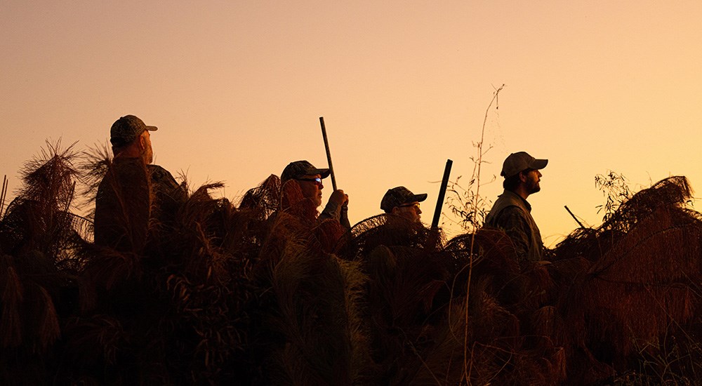 Waterfowl hunters at sunrise silhouetted.